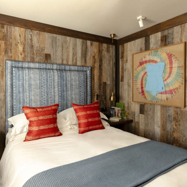 Double bedroom with blue patterned headboard, red cushions, reclaimed wood walls and framed swimsuit artwork at The Gallivant