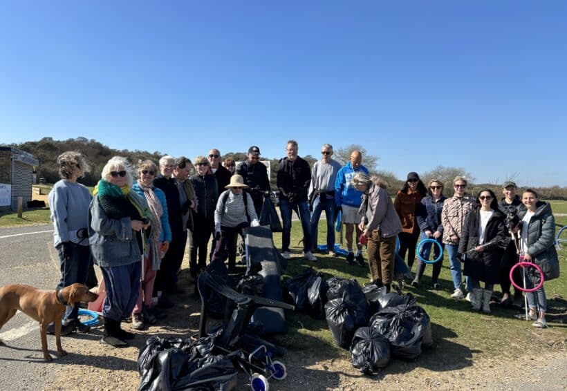 A group of volunteers pose together outdoors on a sunny day beside large black bin bags full of litter collected during a community beach clean